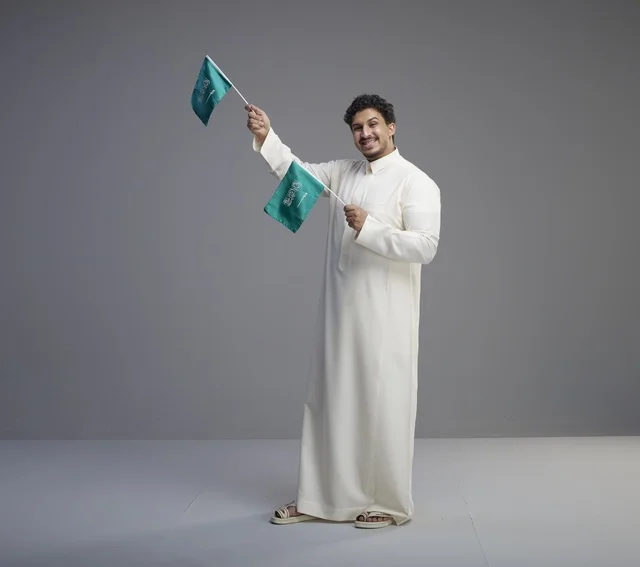 Smiling Saudi Man Holding Small Flags in Gray Studio