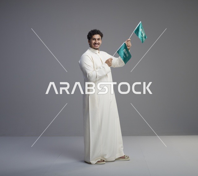 شاب سعودي مبتسم يلوح بعلم المملكة العربية السعودية