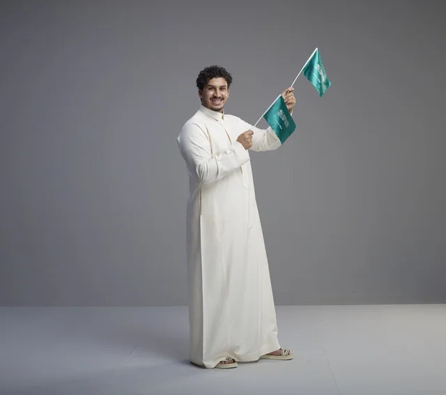 شاب سعودي مبتسم يلوح بعلم المملكة العربية السعودية