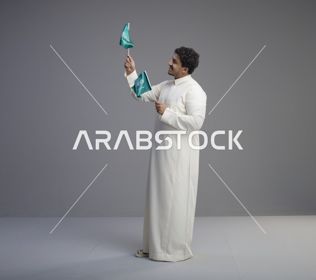 شاب سعودي يرتدي الثوب التقليدي يلوح بعلم السعودية