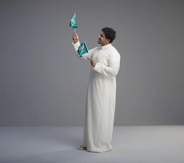 شاب سعودي يرتدي الثوب التقليدي يلوح بعلم السعودية
