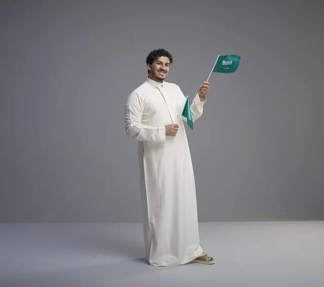 شاب سعودي مبتسم يحمل أعلام المملكة العربية السعودية