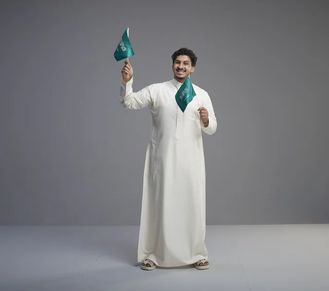 شاب سعودي مبتسم يلوح بعلم السعودية في الاستوديو
