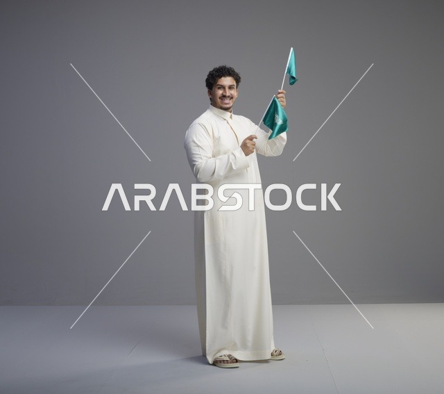 شاب سعودي مبتسم يلوح بأعلام السعودية في الاستوديو