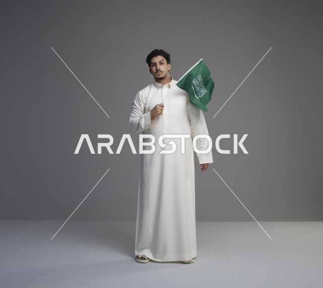شاب سعودي يرتدي الثوب ويحمل علم السعودية
