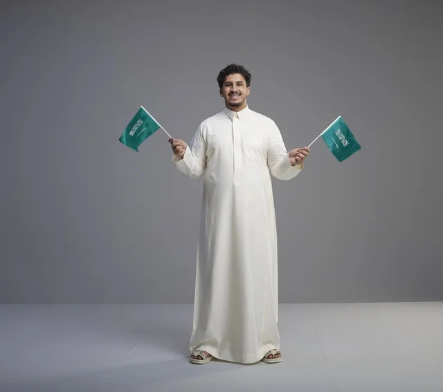 شاب سعودي يرتدي الثوب ويحمل أعلام المملكة