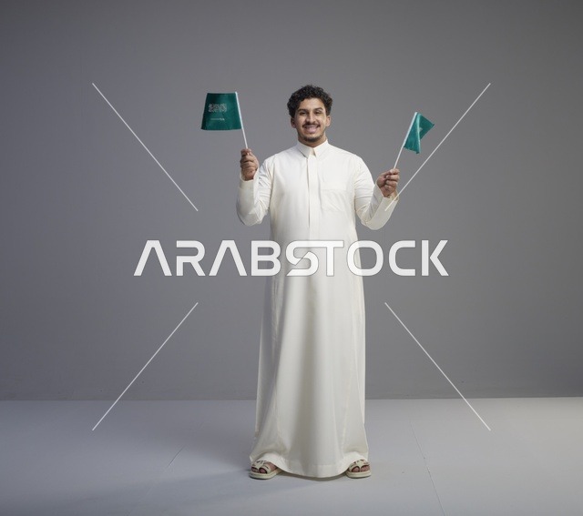 شاب سعودي بالثوب يحمل أعلام المملكة في الاستوديو
