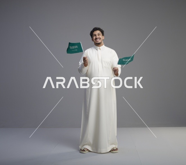 شاب سعودي يبتسم حاملاً أعلام السعودية في الاستوديو