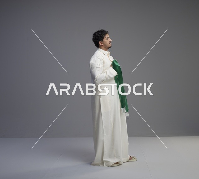 رجل سعودي بالثوب الأبيض يحمل وشاح اليوم الوطني