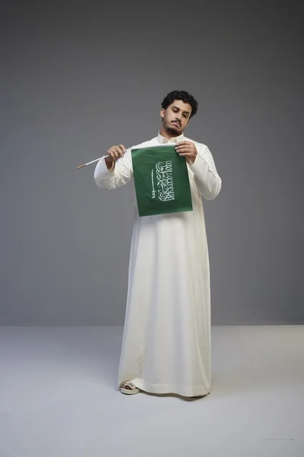 شاب سعودي بالثوب التقليدي يمسك علم السعودية في استوديو