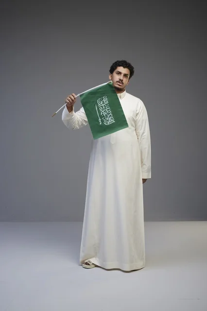 شاب سعودي بالثوب التقليدي يحمل علم المملكة العربية السعودية
