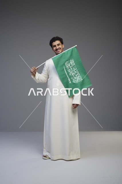 شاب سعودي بالثوب يحمل علم المملكة في استوديو