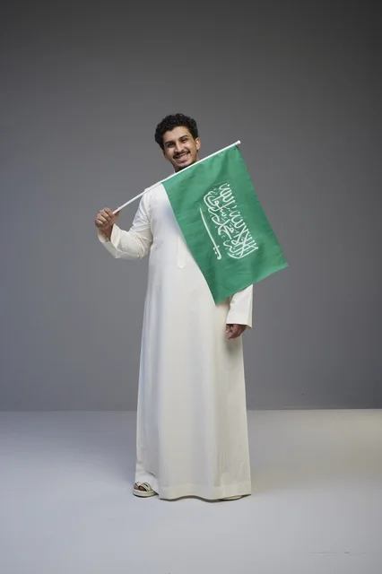شاب سعودي بالثوب يحمل علم المملكة في استوديو