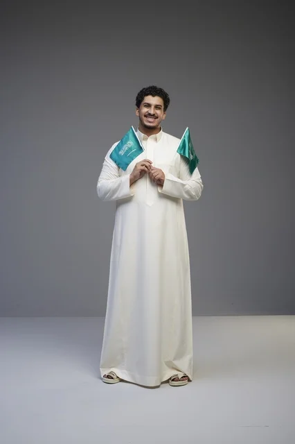 شاب سعودي مبتسم يحمل أعلام السعودية في الاستوديو