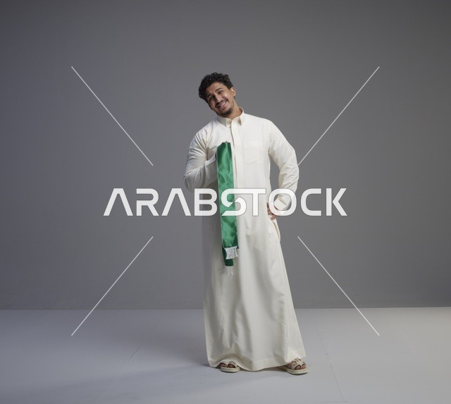رجل سعودي بالثوب الأبيض يحمل وشاحاً وطنياً أخضر