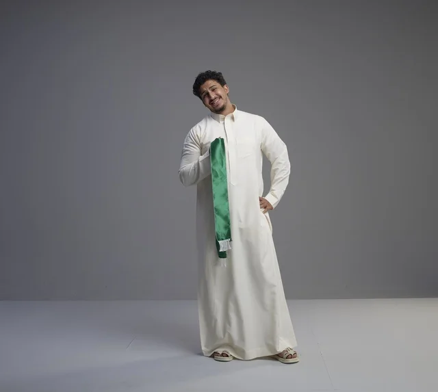 رجل سعودي بالثوب الأبيض يحمل وشاحاً وطنياً أخضر