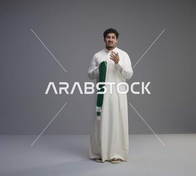 رجل سعودي بالثوب الأبيض يحمل وشاحاً وطنياً أخضر