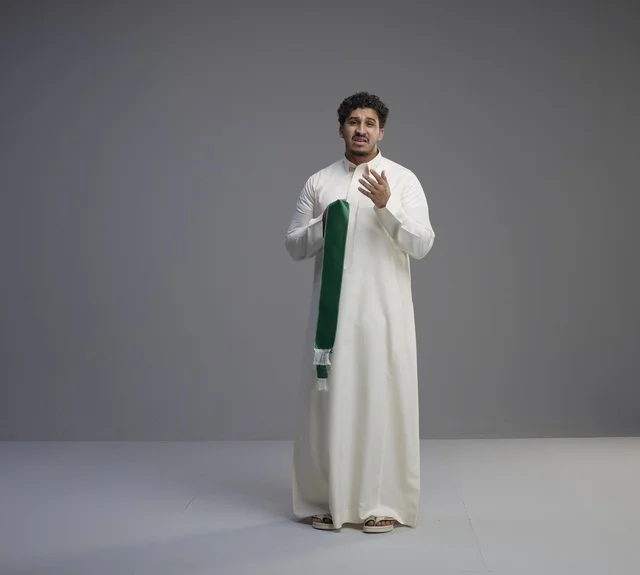 رجل سعودي بالثوب الأبيض يحمل وشاحاً وطنياً أخضر