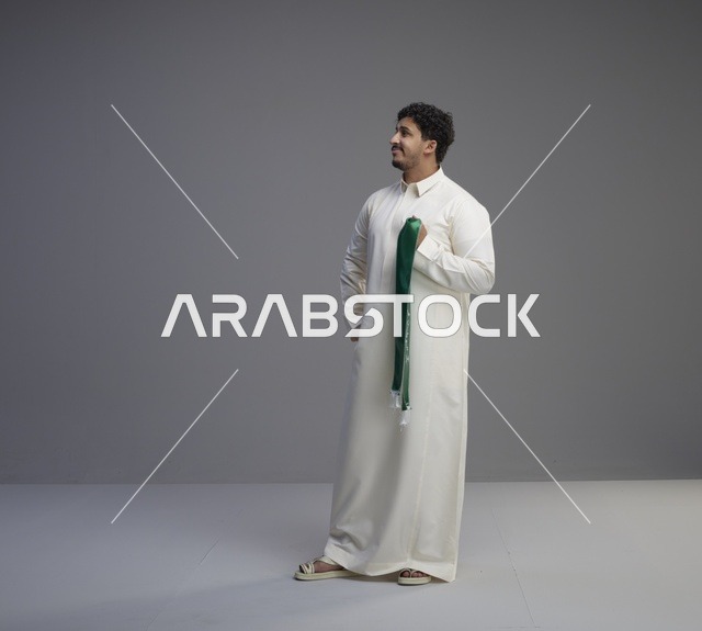 رجل سعودي بالثوب الأبيض يحمل وشاحاً وطنياً أخضر