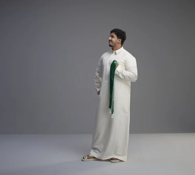 رجل سعودي بالثوب الأبيض يحمل وشاحاً وطنياً أخضر