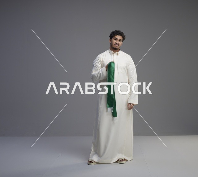 رجل سعودي بالثوب الأبيض يحمل وشاحاً وطنياً أخضر