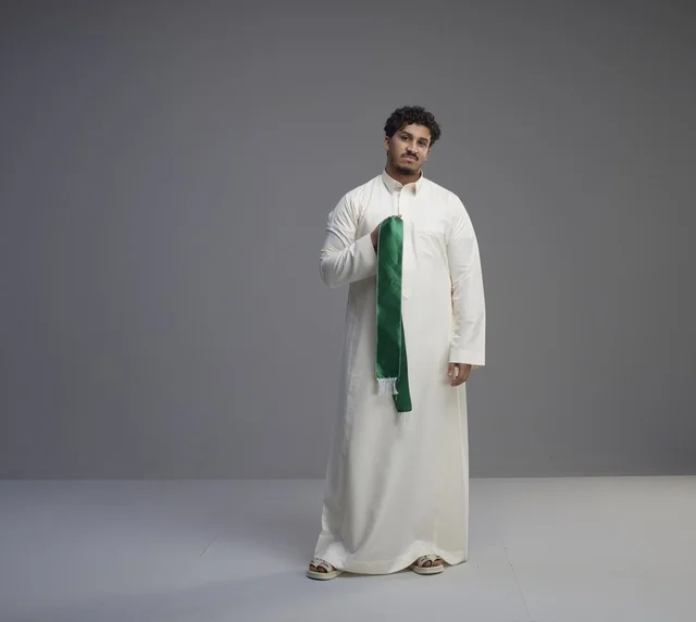 رجل سعودي بالثوب الأبيض يحمل وشاحاً وطنياً أخضر