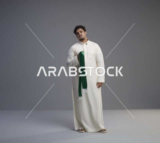 رجل سعودي بالثوب الأبيض يحمل وشاحاً وطنياً أخضر