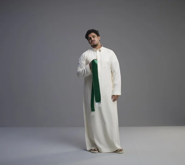 رجل سعودي بالثوب الأبيض يحمل وشاحاً وطنياً أخضر