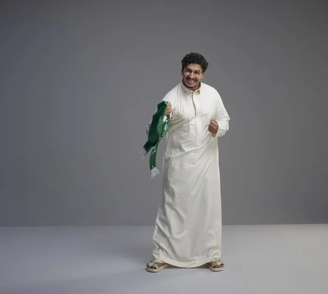 رجل سعودي يحمل وشاحاً وطنياً ويحتفل في الاستوديو