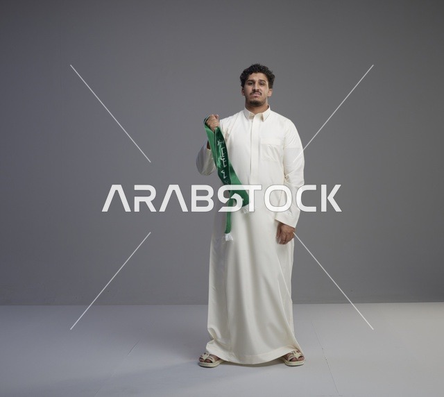 رجل سعودي بالثوب الأبيض يحمل وشاحاً وطنياً أخضر