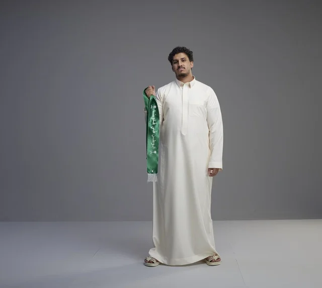 رجل سعودي يحمل وشاحاً وطنياً أخضر في الاستوديو