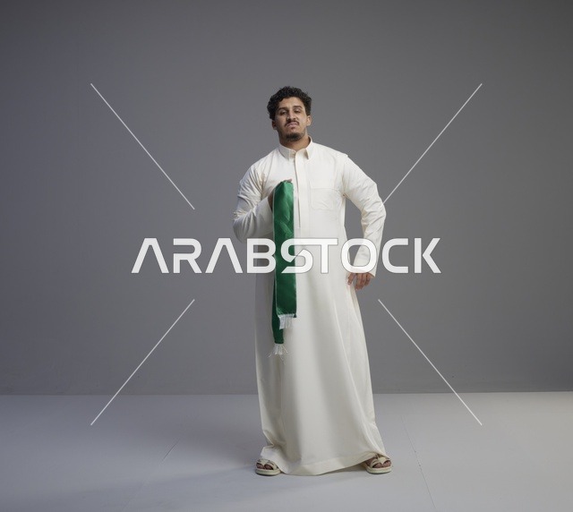 رجل سعودي بالثوب يحمل وشاح اليوم الوطني