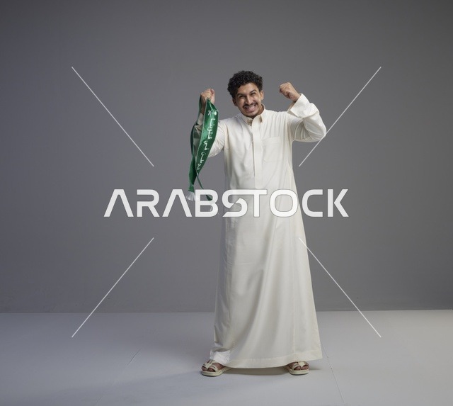 رجل سعودي بالثوب يحمل وشاحاً وطنياً في استوديو