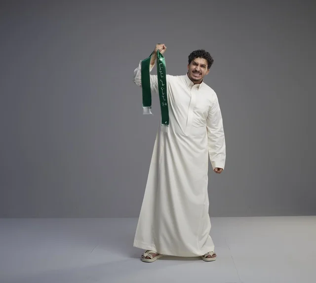 رجل سعودي يحمل وشاحاً وطنياً أخضر يحتفل باليوم الوطني