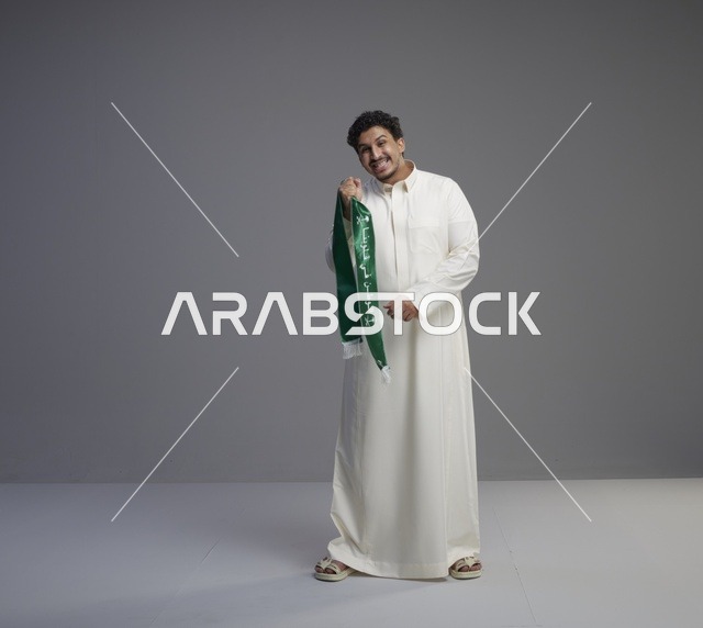 رجل سعودي بالثوب الأبيض يحمل الوشاح الوطني