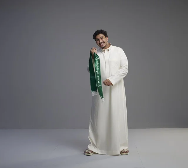 رجل سعودي بالثوب الأبيض يحمل الوشاح الوطني