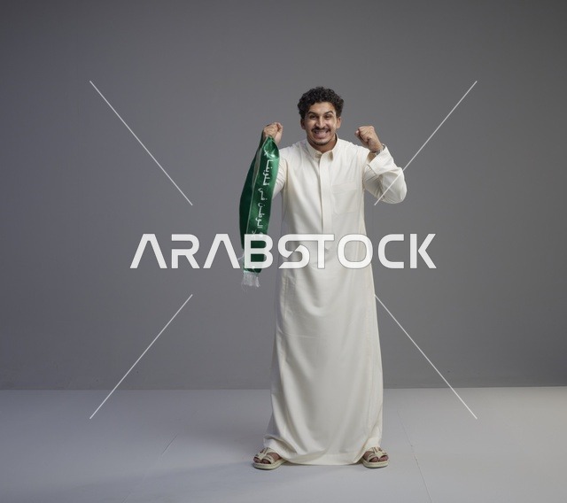 رجل سعودي يرتدي الثوب الأبيض ويحمل وشاحاً وطنياً