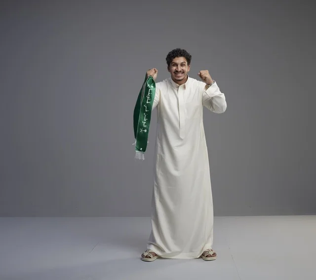 رجل سعودي يرتدي الثوب الأبيض ويحمل وشاحاً وطنياً