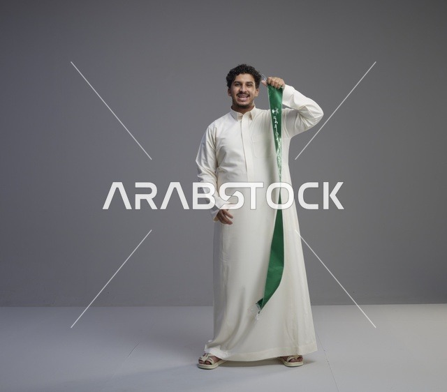 رجل سعودي بالثوب الأبيض يحمل وشاحاً وطنياً