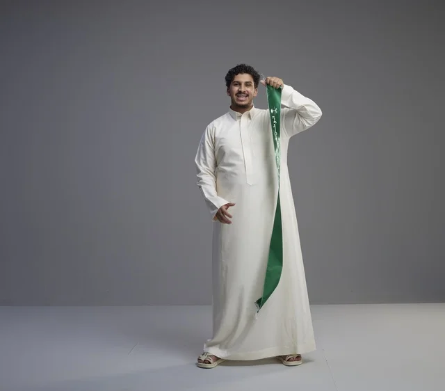 رجل سعودي بالثوب الأبيض يحمل وشاحاً وطنياً