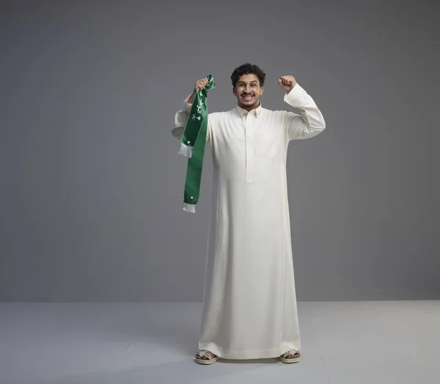رجل سعودي بالثوب التقليدي يحمل وشاحاً وطنياً أخضر