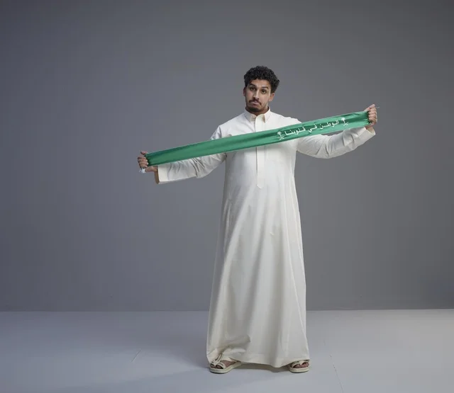 رجل سعودي يحمل وشاحاً وطنياً أخضر في الاستوديو