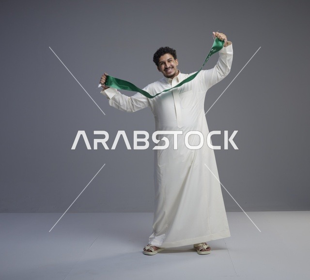 رجل سعودي بالثوب الأبيض يحمل وشاح اليوم الوطني