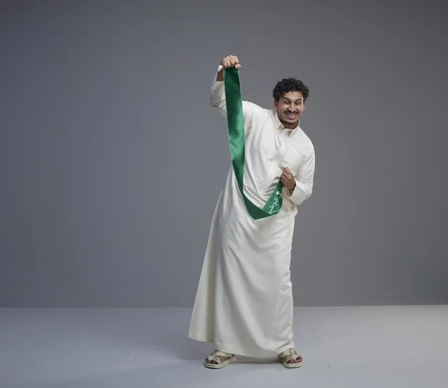 رجل سعودي بالثوب الأبيض يحمل وشاح اليوم الوطني
