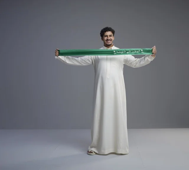 رجل سعودي يرتدي الثوب ويحمل الوشاح الوطني الأخضر