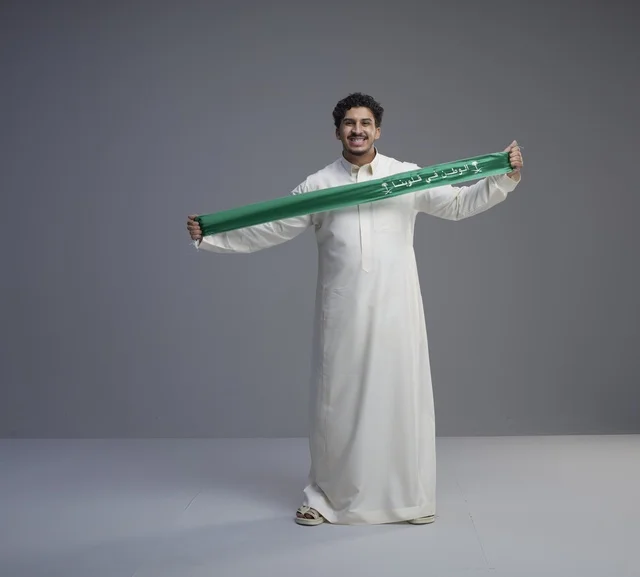 رجل سعودي يحمل وشاحاً وطنياً أخضر في استوديو