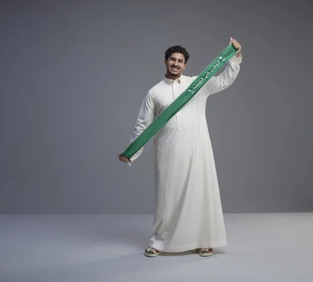 رجل سعودي يحمل وشاحاً وطنياً أخضر في الاستوديو