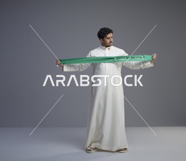 رجل سعودي بالثوب يحمل وشاحاً وطنياً أخضر