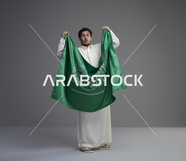 رجل سعودي بالثوب يحمل العلم الوطني في الاستوديو