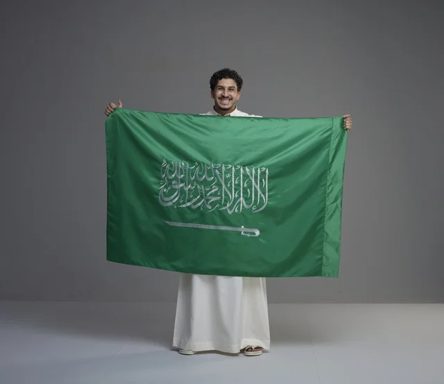 Saudi Man Holding National Flag in Gray Studio Setting